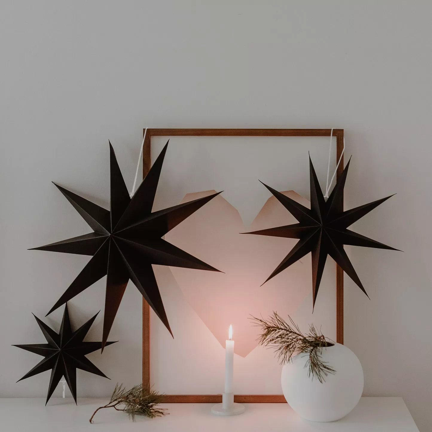 Three black paper stars as wall decorations with candles and picture frames – stylish Christmas atmosphere in the interior.