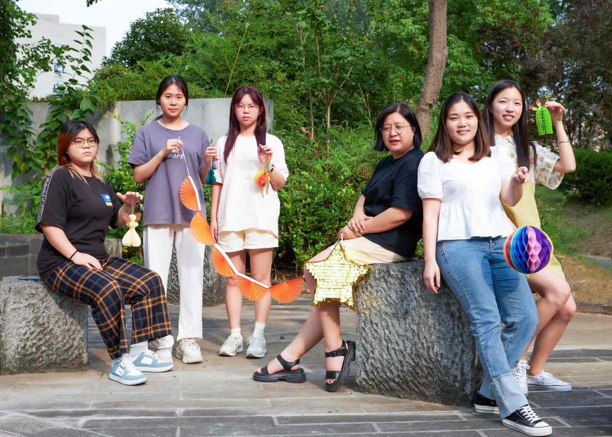 Sunbeauty Sales Team pose outdoors with colorful paper honeycomb decorations, green foliage backdrop.