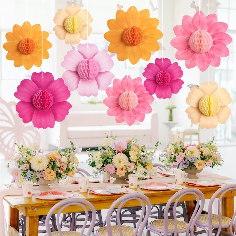 3D honeycomb paper flower ornaments hanging above decorated wooden dining table, floral table setting for garden party