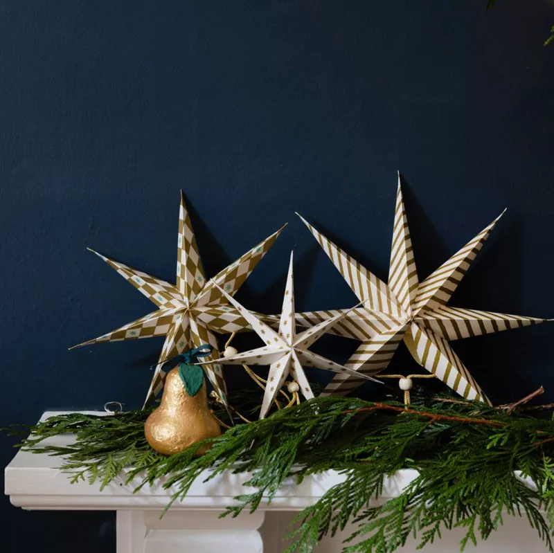 Close-up view of three multi-point hanging paper stars, gold white stripe and checker print, gold hanging cords, white isolated background