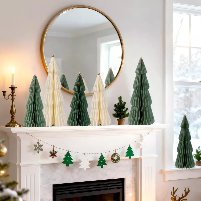 Dark green and cream accordion paper Christmas trees with gold ball toppers arranged on white marble fireplace mantel, Christmas garland and round gold mirror backdrop