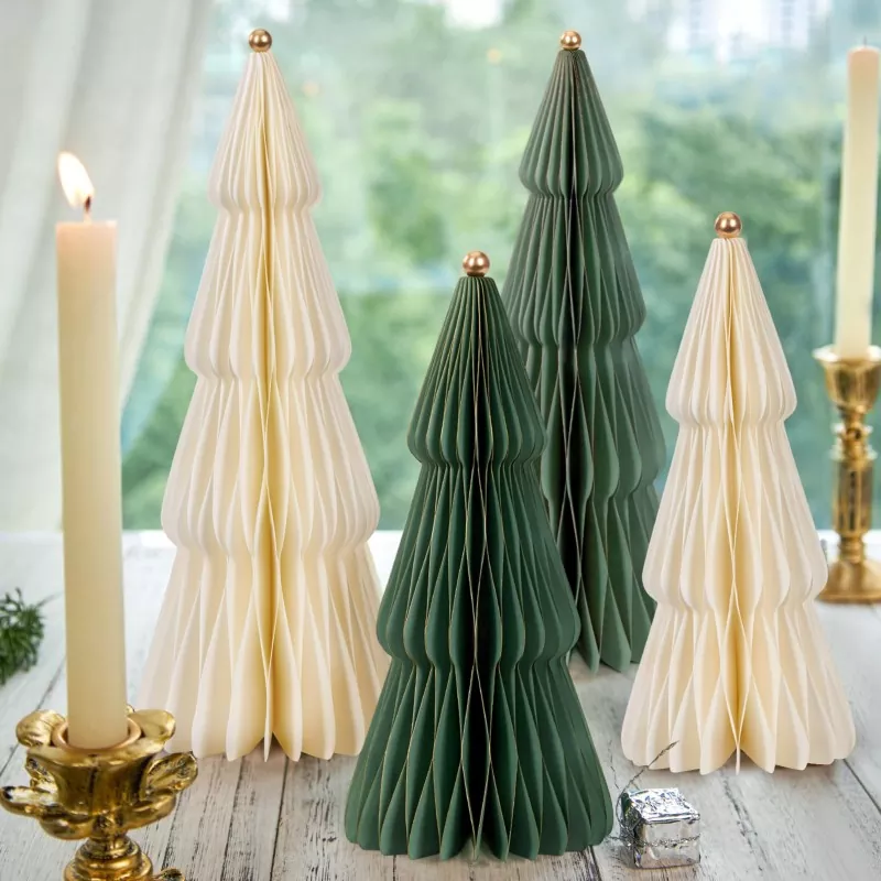 Dark green and cream accordion paper Christmas trees with gold tops arranged on rustic wooden table, paired with tall pillar candles in brass holders
