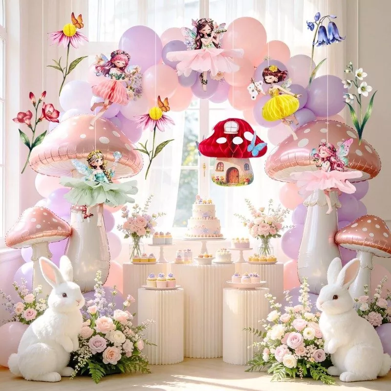 Fairy theme birthday party backdrop setup with hanging fairy cutouts, mushroom foil balloons, cake table and white bunny decorations