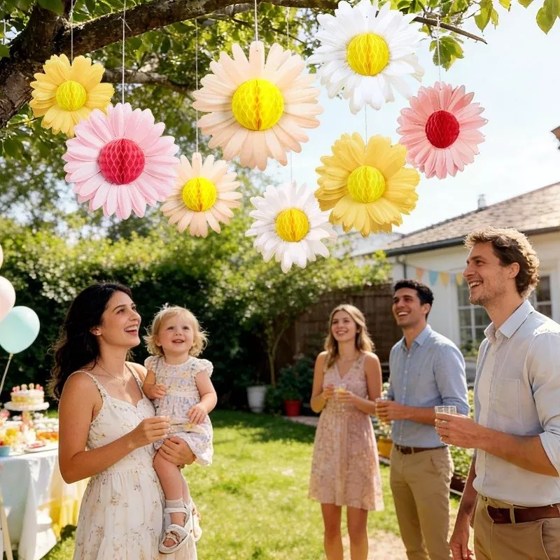 Family garden party with hanging pink, white and yellow daisy honeycomb paper flower decorations hanging from tree branches