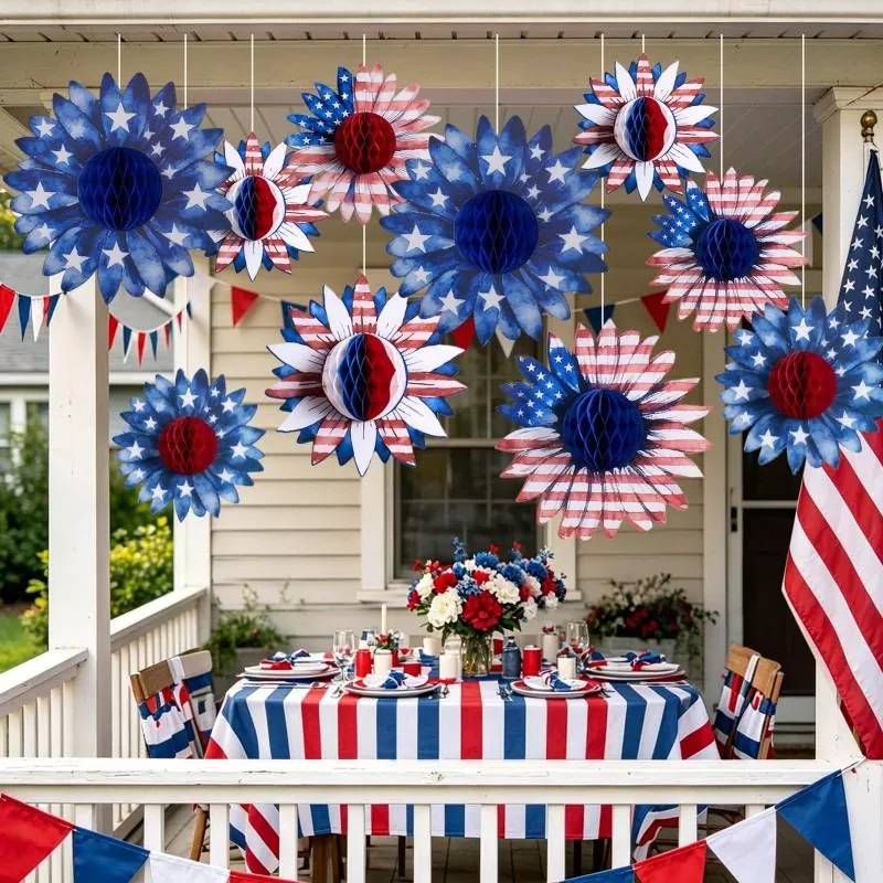 Hanging red white blue sunflower honeycomb paper flowers on front porch for 4th of July outdoor dinner party with flag and bunting