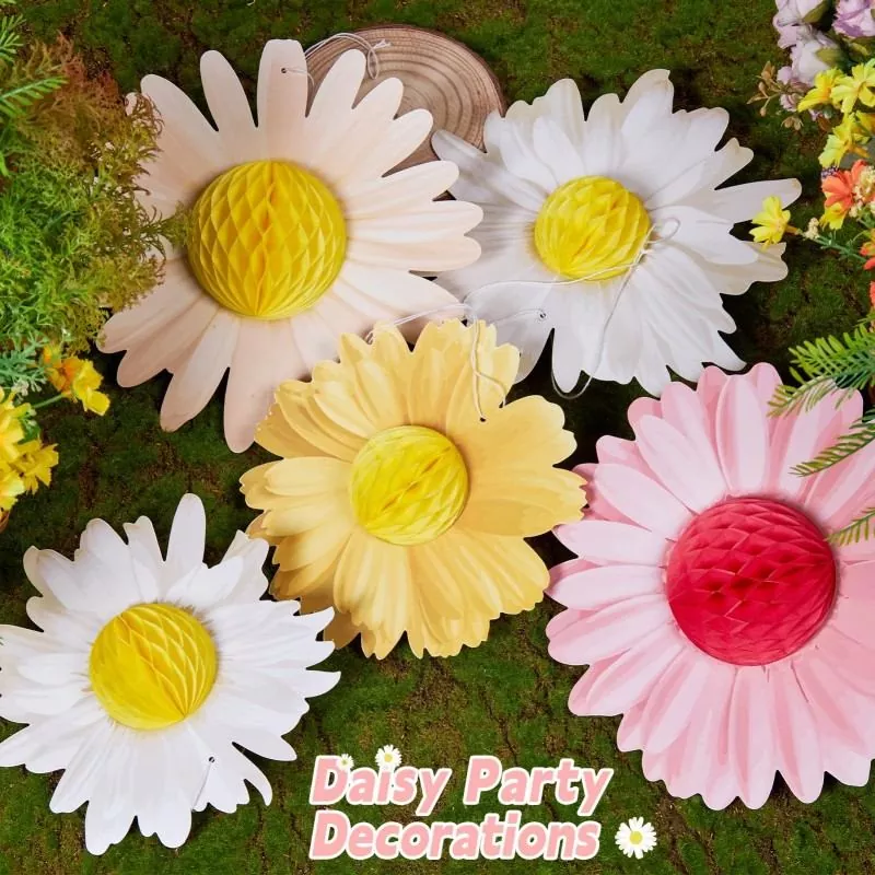 Pink cream white yellow daisy honeycomb paper flower cutouts laid on green moss, daisy party decorations text