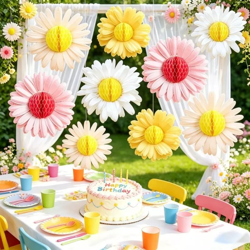 Pink white yellow daisy honeycomb paper flower hanging ornaments above outdoor garden birthday table with cake and colorful tableware