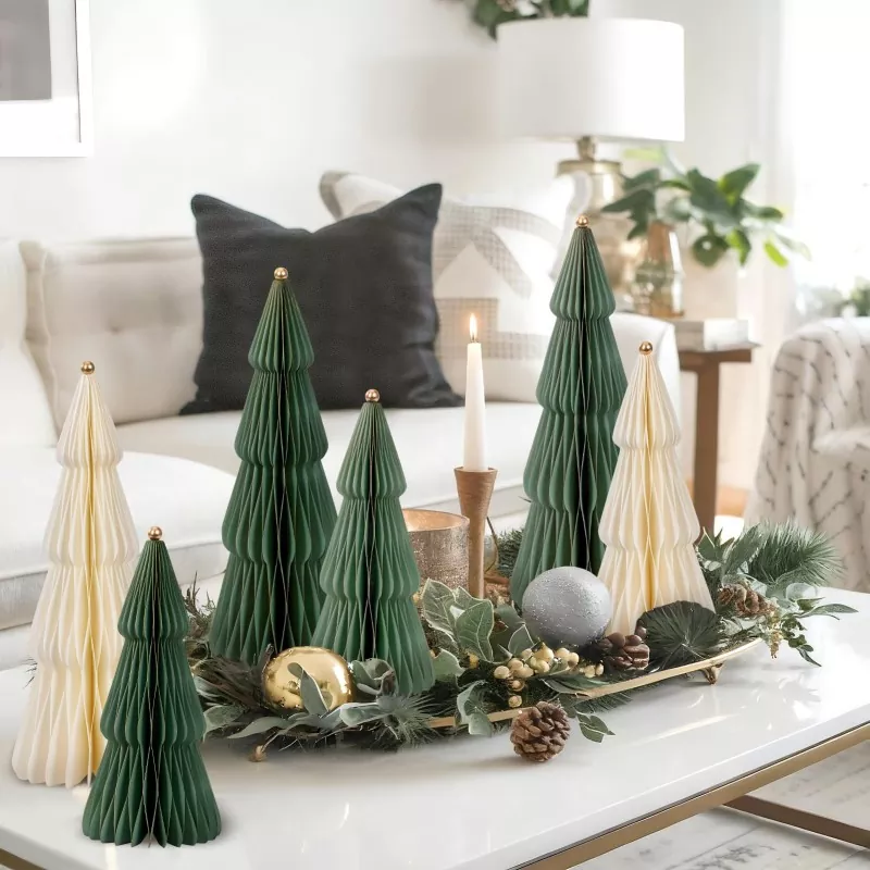 Pleated paper Christmas trees in green and cream placed on white coffee table, styled with pinecones, green foliage, ornaments and candle for modern home Christmas decor
