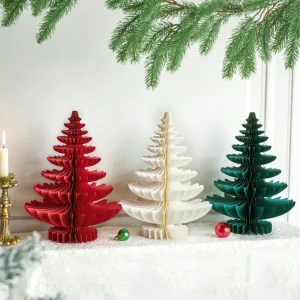 Red, white, green honeycomb foldable paper Christmas tabletop trees, arranged on white linen surface with candle and pine sprigs